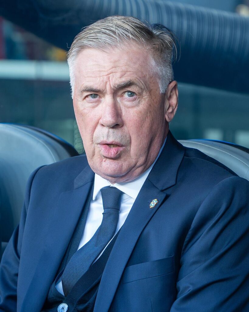 Carlo Ancelotti in a dark blue suit and tie, sitting on the Brazil bench at the 2026 World Cup