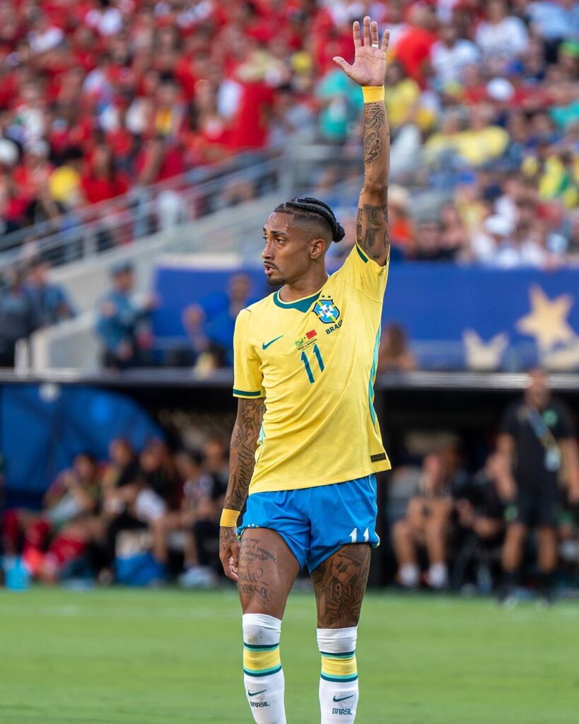 Raphinha in Brazil's number 11 shirt, raising his hand on the pitch