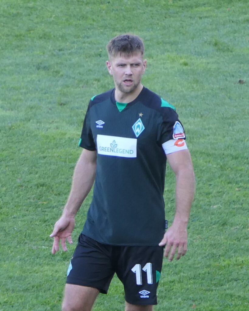 Niclas Füllkrug in a dark green Werder Bremen kit, number 11, standing on the pitch