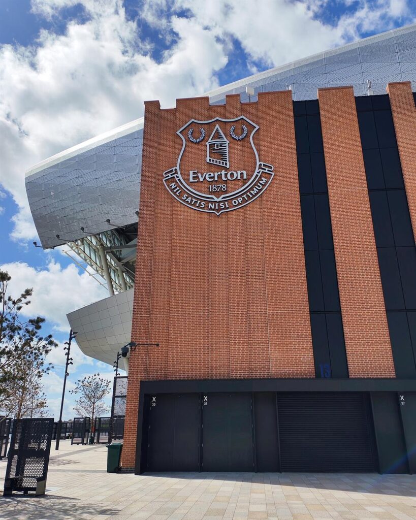 The Everton crest on the brick wall of Hill Dickinson Stadium under a blue sky