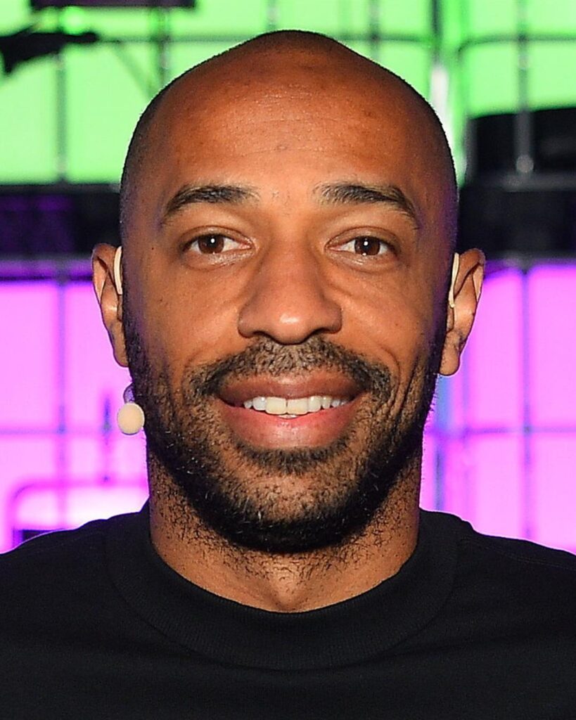 Thierry Henry smiling on stage at a conference, in a black top