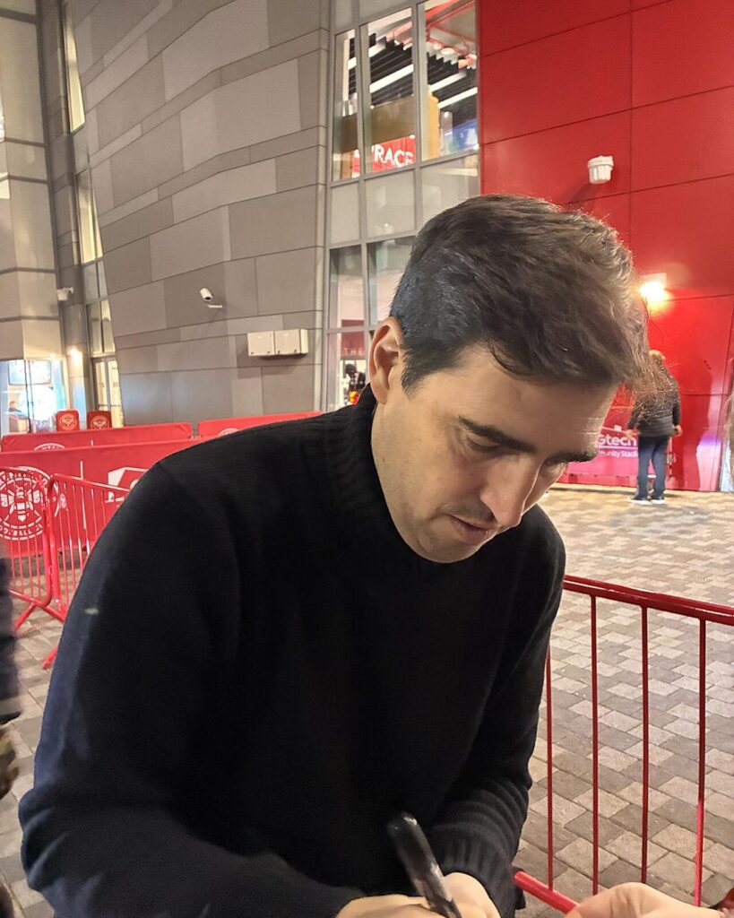 Andoni Iraola in a dark jumper, signing an autograph outside a stadium