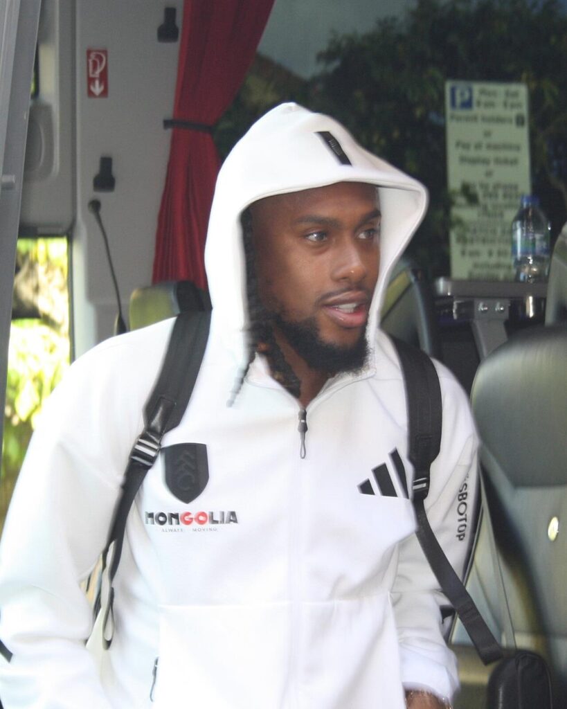 Alex Iwobi in a white Fulham hooded training top, getting off the team bus