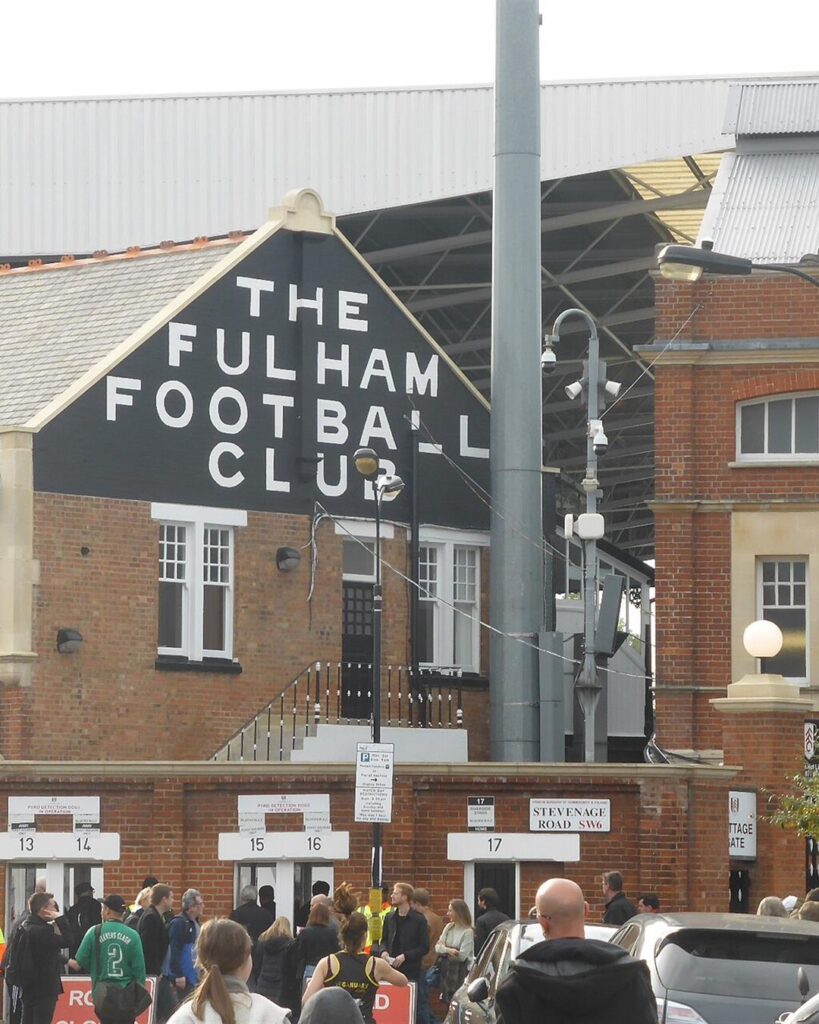 Fans outside Craven Cottage on a match day, with The Fulham Football Club painted on the building