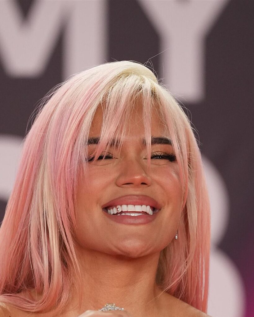 Karol G with pink hair smiling on the red carpet at the 2023 Latin Grammy Awards