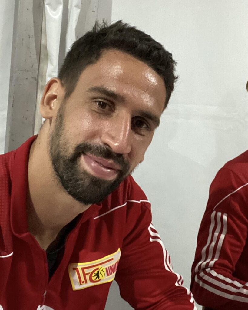 Rani Khedira smiling in a red 1. FC Union Berlin training top at an autograph session