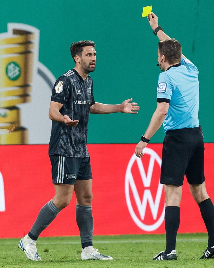 Rani Khedira talking to the referee in a German Cup game in a dark Union Berlin kit