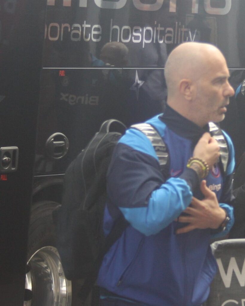 Enzo Maresca in a blue training jacket, carrying a backpack next to a team bus
