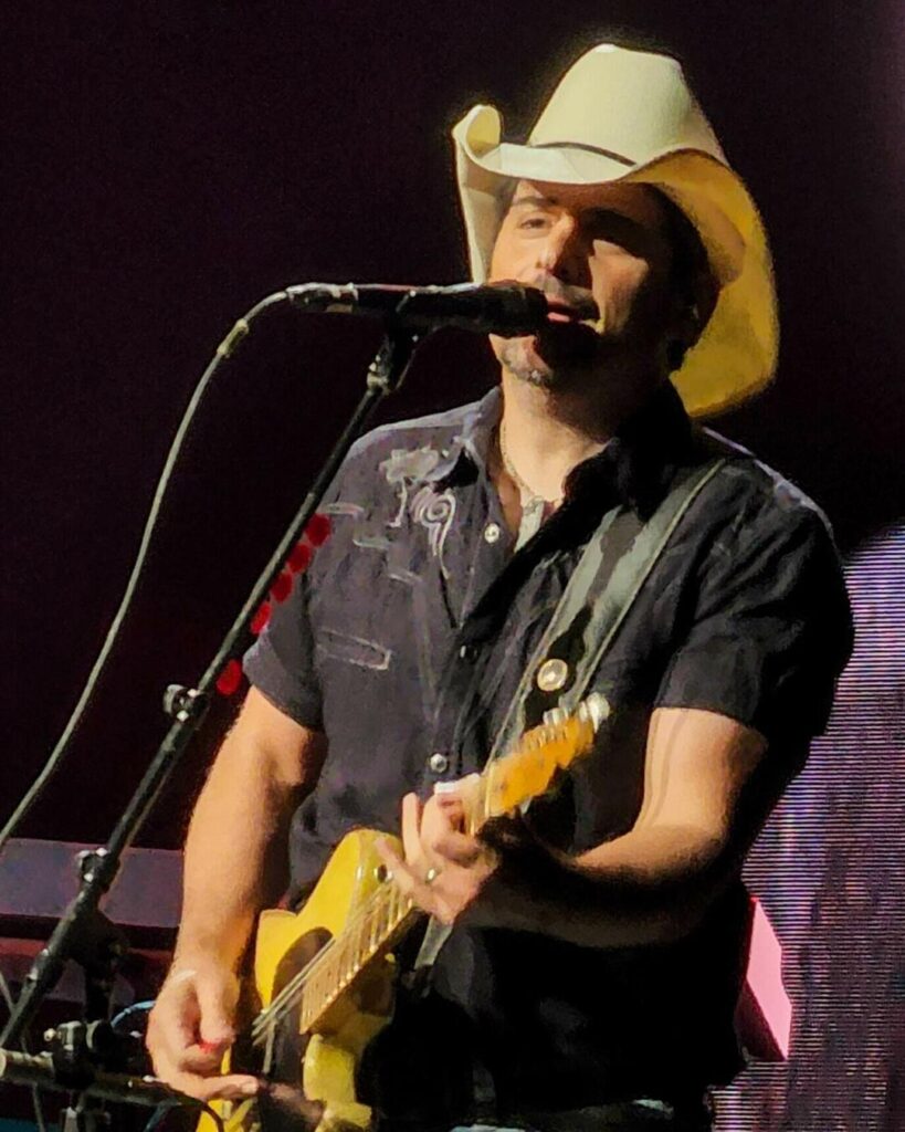 Brad Paisley in a white cowboy hat singing and playing guitar on stage, 2022