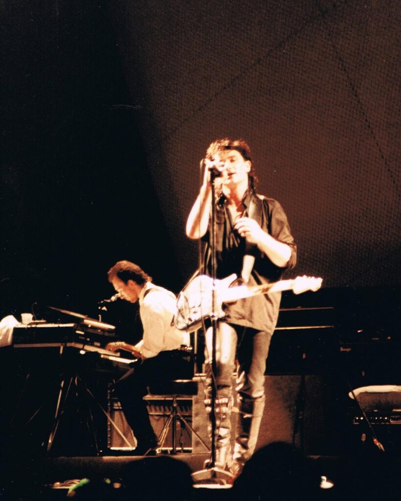 A young Bono singing with a guitar on stage in Sydney in 1984